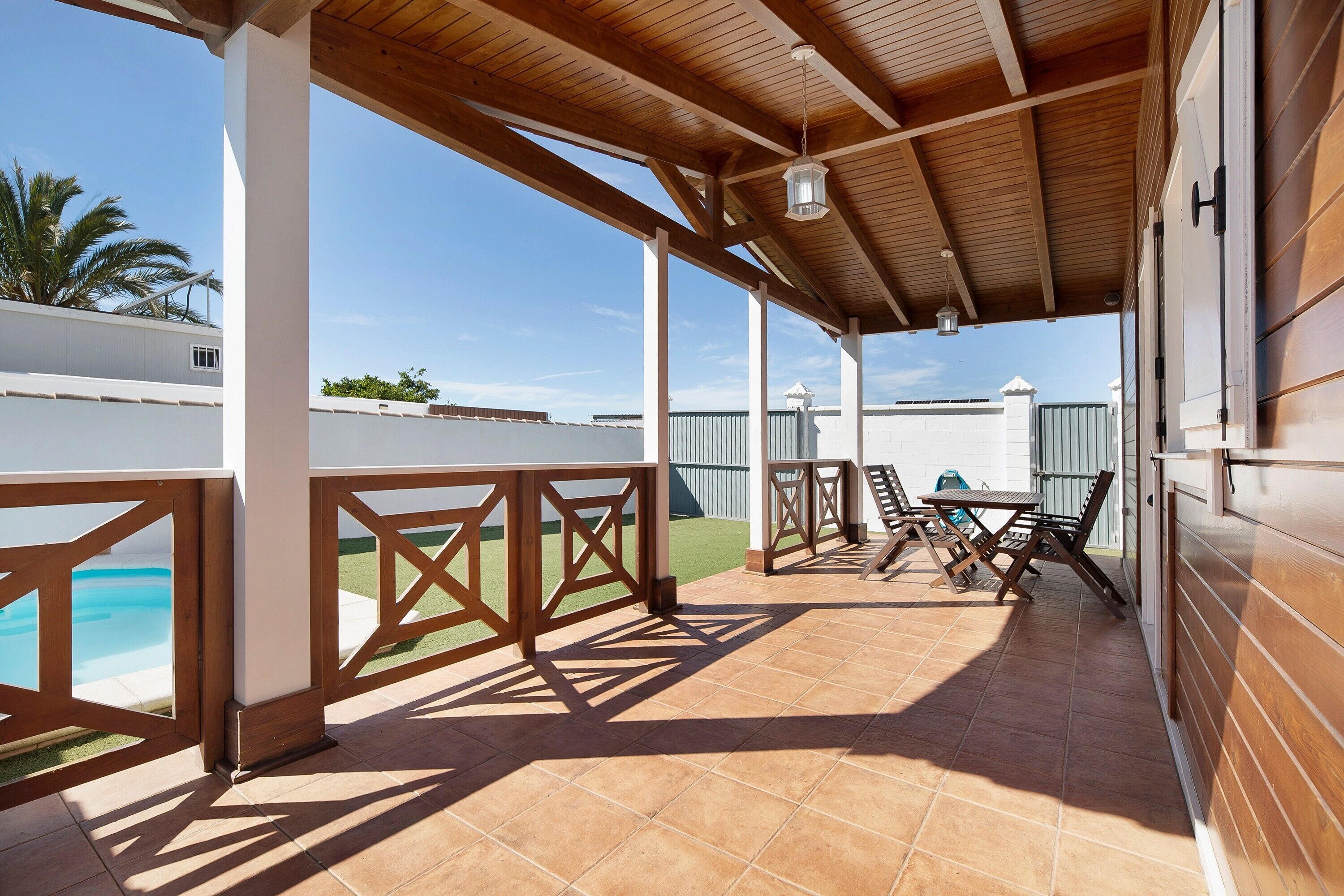 A covered outdoor area with a pool, wooden furniture, and a view of the sky.