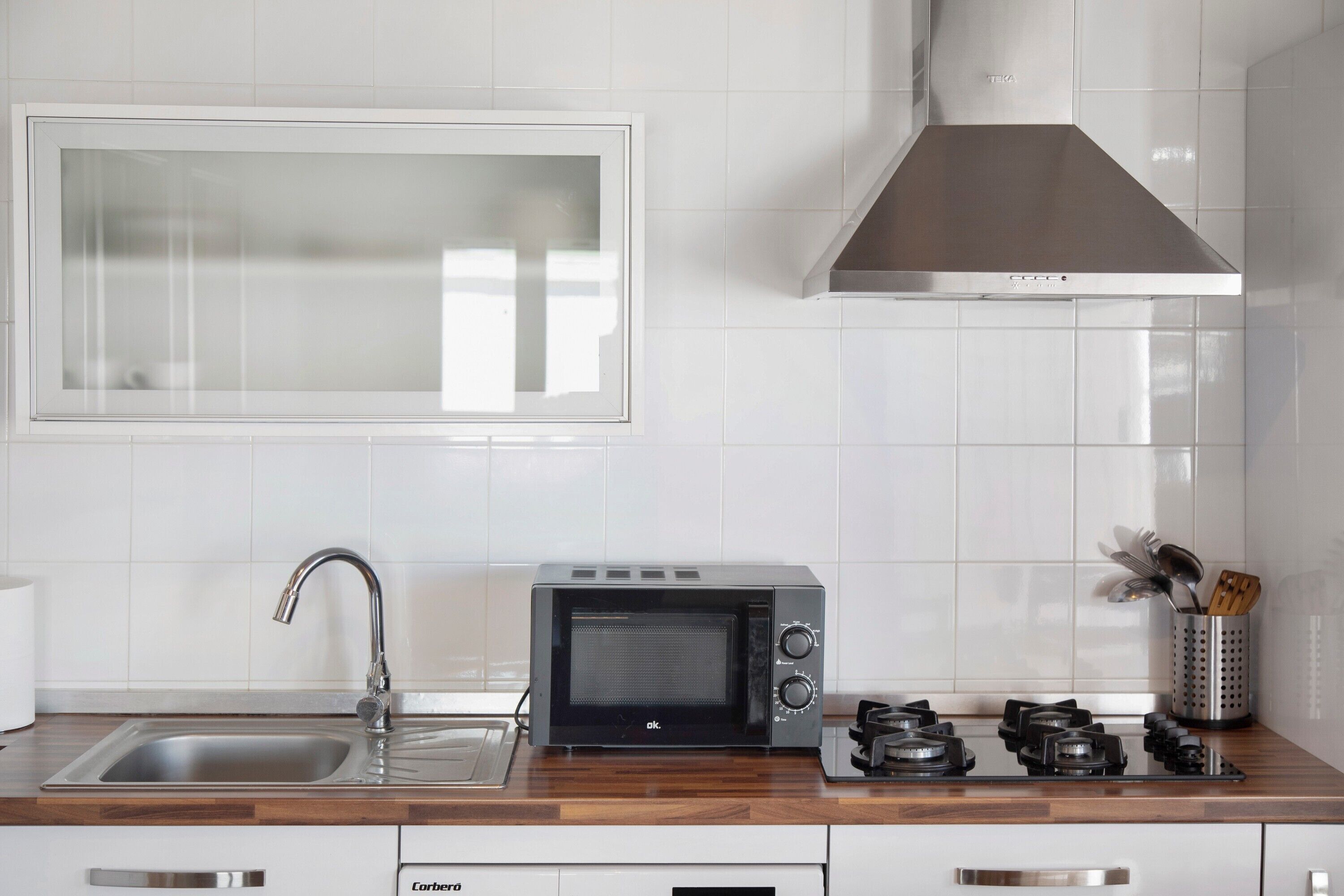 A kitchen with a microwave, sink, stove, and stainless steel cabinets.
