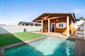 Una propiedad residencial con piscina, terraza de madera y zona de patio cubierta.