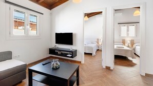 Ein modernes Zimmer mit Flachbildfernseher, einer Couch, einem Couchtisch und einem Bett mit Nachttisch.
