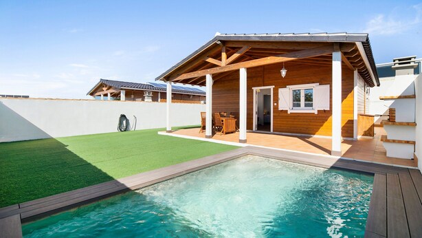 Ein Wohnhaus mit Schwimmbad, Holzdeck und überdachter Terrasse.