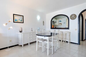 A dining area with a round table, white chairs, a white cabinet, a framed picture, and a mirror.