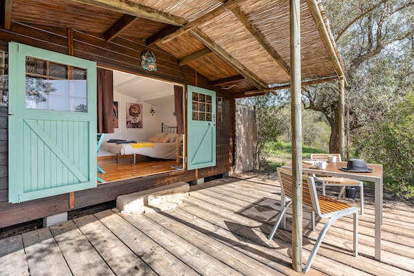 A wooden deck with a covered seating area, a table with chairs, and a view of the surrounding landscape.