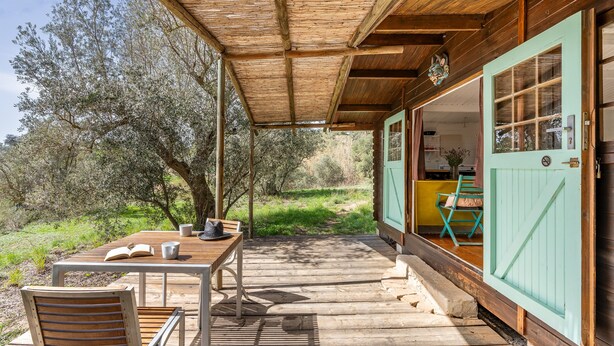 Een houten terras met een tafel en stoelen, een overdekt gedeelte en een gebouw met een groene deur.