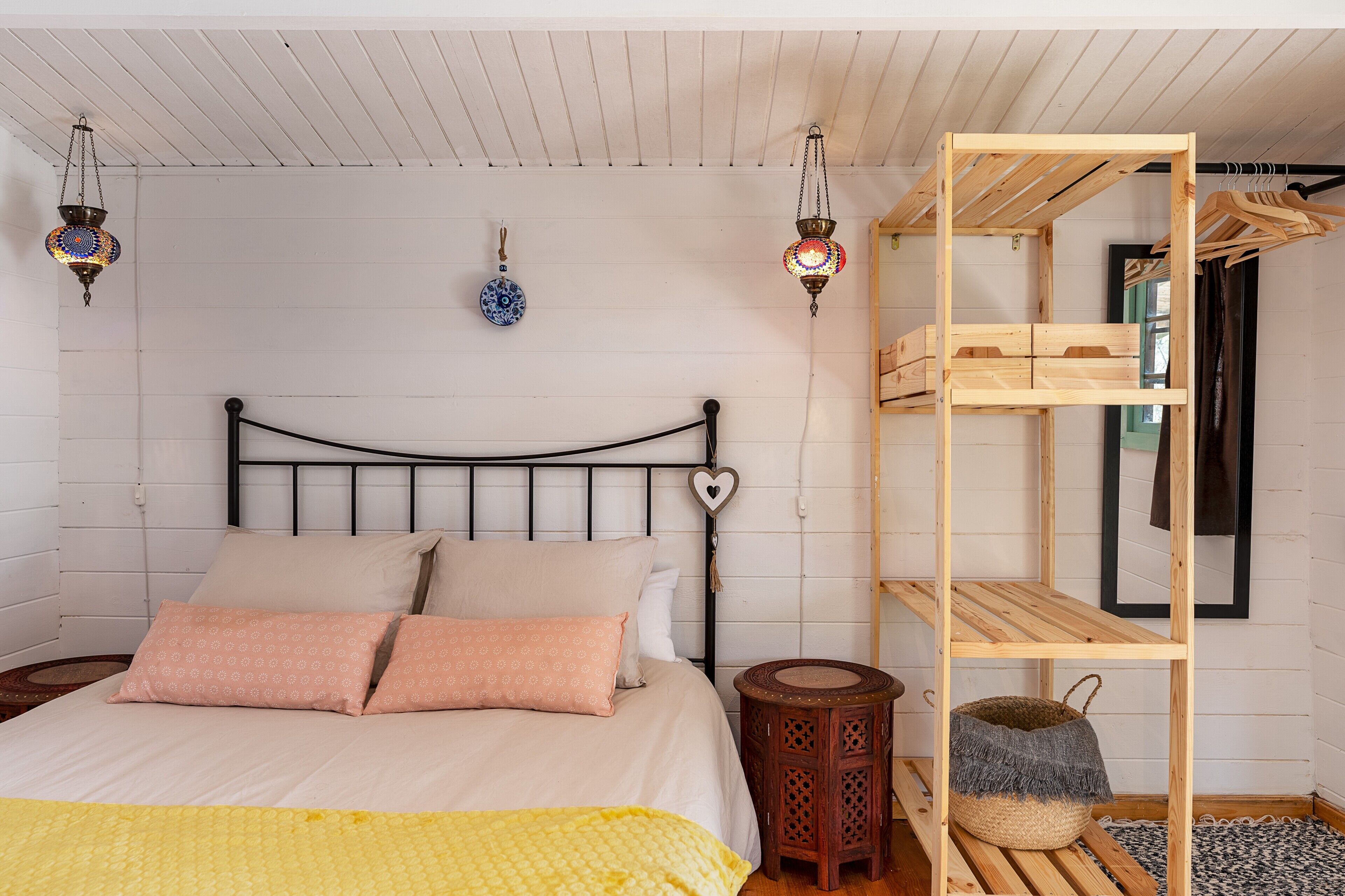 Una cama con cabecera, una estantería de madera y dos faroles colgantes.