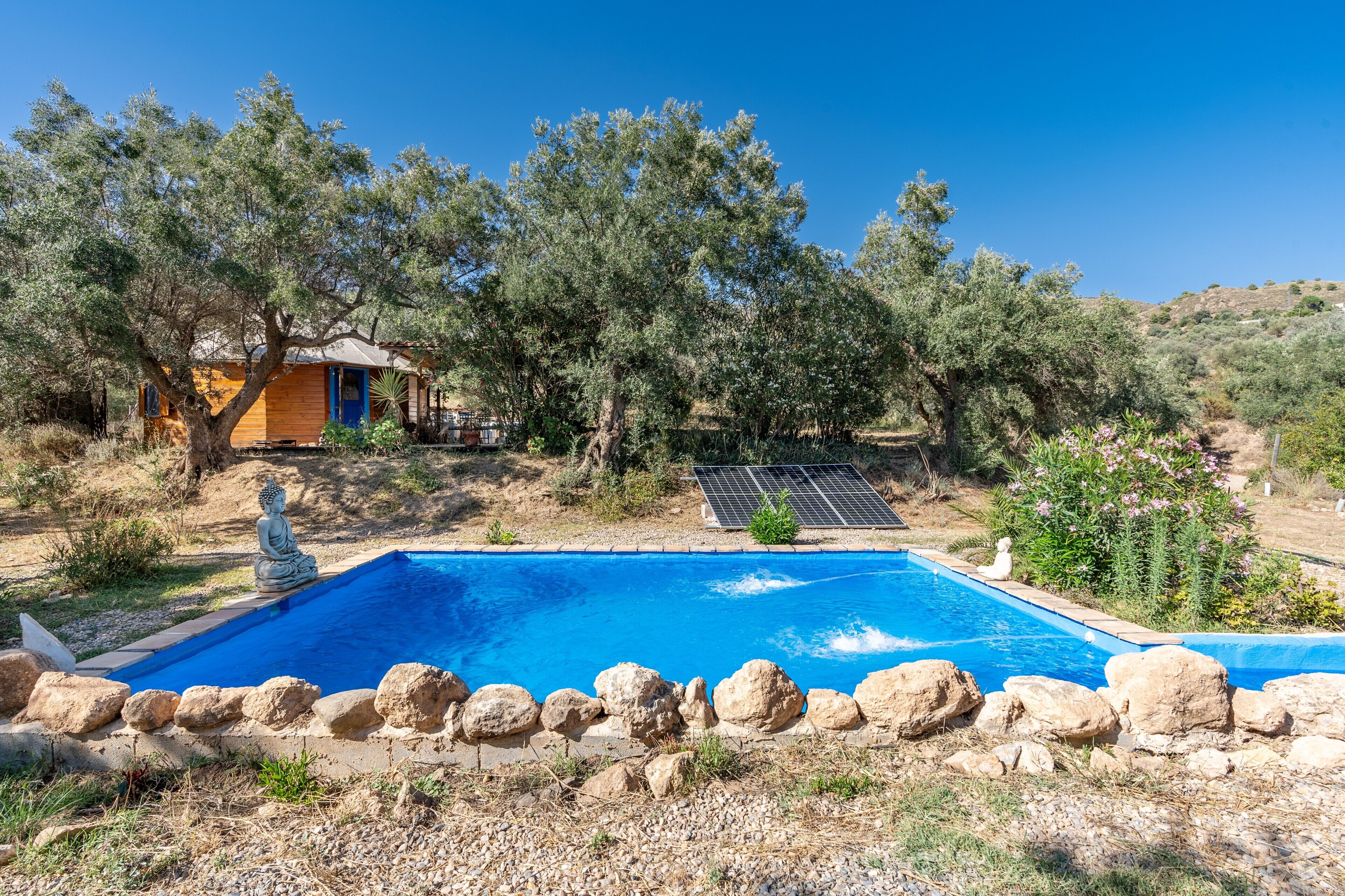 A swimming pool surrounded by rocks, a statue, and a small building with a blue door.