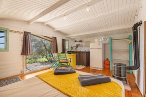 A cozy room with a bed, a chair, a small kitchen, and a view of the outdoors.