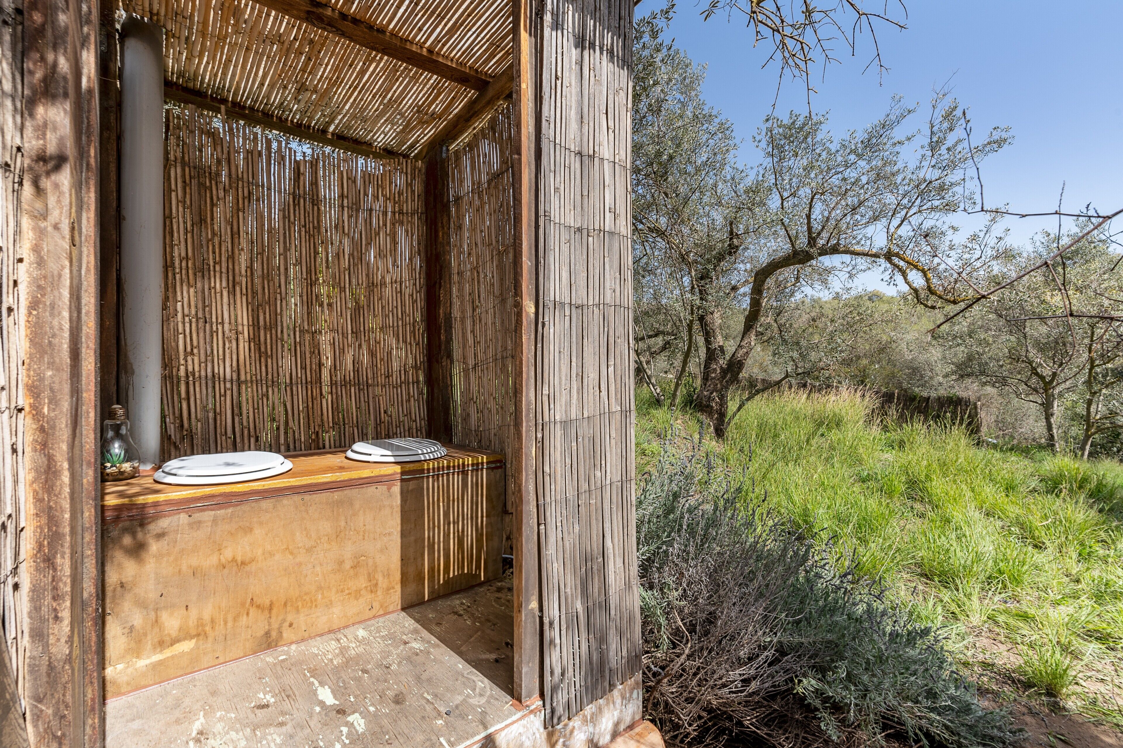 Una estructura de madera con pared de bambú y un banco con un plato.