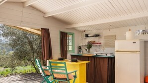 Een kleine keuken met een houten tafel, een stoel, een koelkast en een raam met uitzicht op groen.