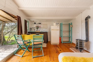 A cozy kitchen with wooden floors, a dining table with chairs, a refrigerator, and a wood-burning stove.