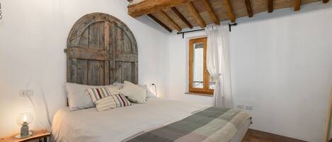 Ein Schlafzimmer mit Holztür, einem Bett mit gestreifter Decke, einem Nachttisch mit Lampe und einem Fenster mit Vorhängen.