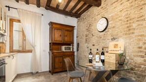 A kitchen with a wooden cabinet, a microwave, and a glass table with chairs. - Apartment 'Domus Vestae' with Wi-Fi and Air Conditioning (San Gimignano)
