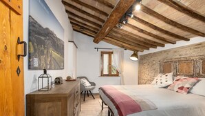 A bedroom with a wooden ceiling, a bed with a patterned bedspread, a desk with a lamp, a chair, and a stone wall. - Apartment 'Domus Vestae' with Wi-Fi and Air Conditioning (San Gimignano)