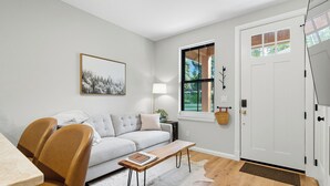 A modern living room with a sofa, chairs, a coffee table, a lamp, and a door with a window.