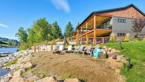 A modern house with a large deck overlooking a lake, surrounded by rocks and greenery.