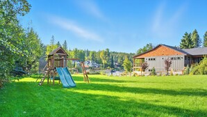 A grassy backyard with a wooden playhouse and a slide.