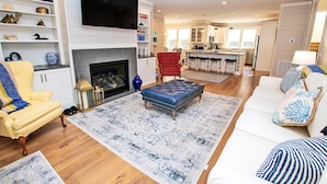 A spacious living room with a fireplace, a television, and a dining area with bar stools. - Soundside, Private Pool, Den, Yard, Screened Porch, SH106, Turners Tide (Duck)