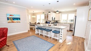 A modern kitchen with white cabinetry, a central island with bar stools, and pendant lighting. - Soundside, Private Pool, Den, Yard, Screened Porch, SH106, Turners Tide (Duck)