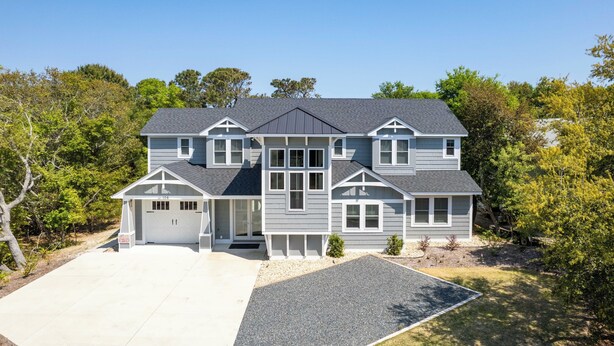 A two-story house with a garage, surrounded by trees and a well-maintained lawn. - Soundside, Private Pool, Den, Yard, Screened Porch, SH106, Turners Tide (Duck)