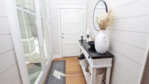 A narrow hallway with a glass door leading to a balcony, a white door, a black countertop with a vase and candles, and a small white shelf with baskets. - Soundside, Private Pool, Den, Yard, Screened Porch, SH106, Turners Tide (Duck)