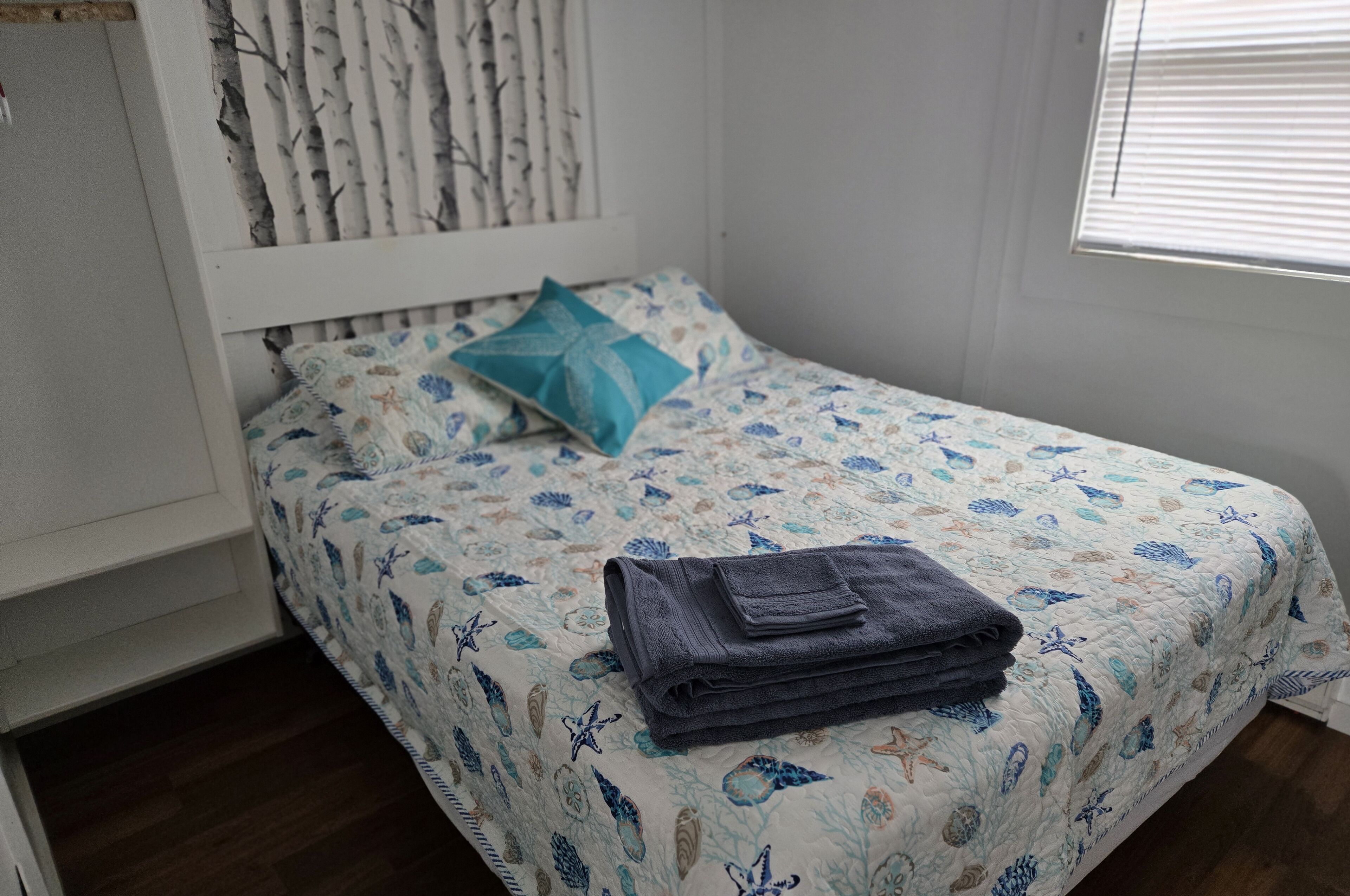 A neatly made bed with a floral bedspread, a folded towel, and a single teal pillow.