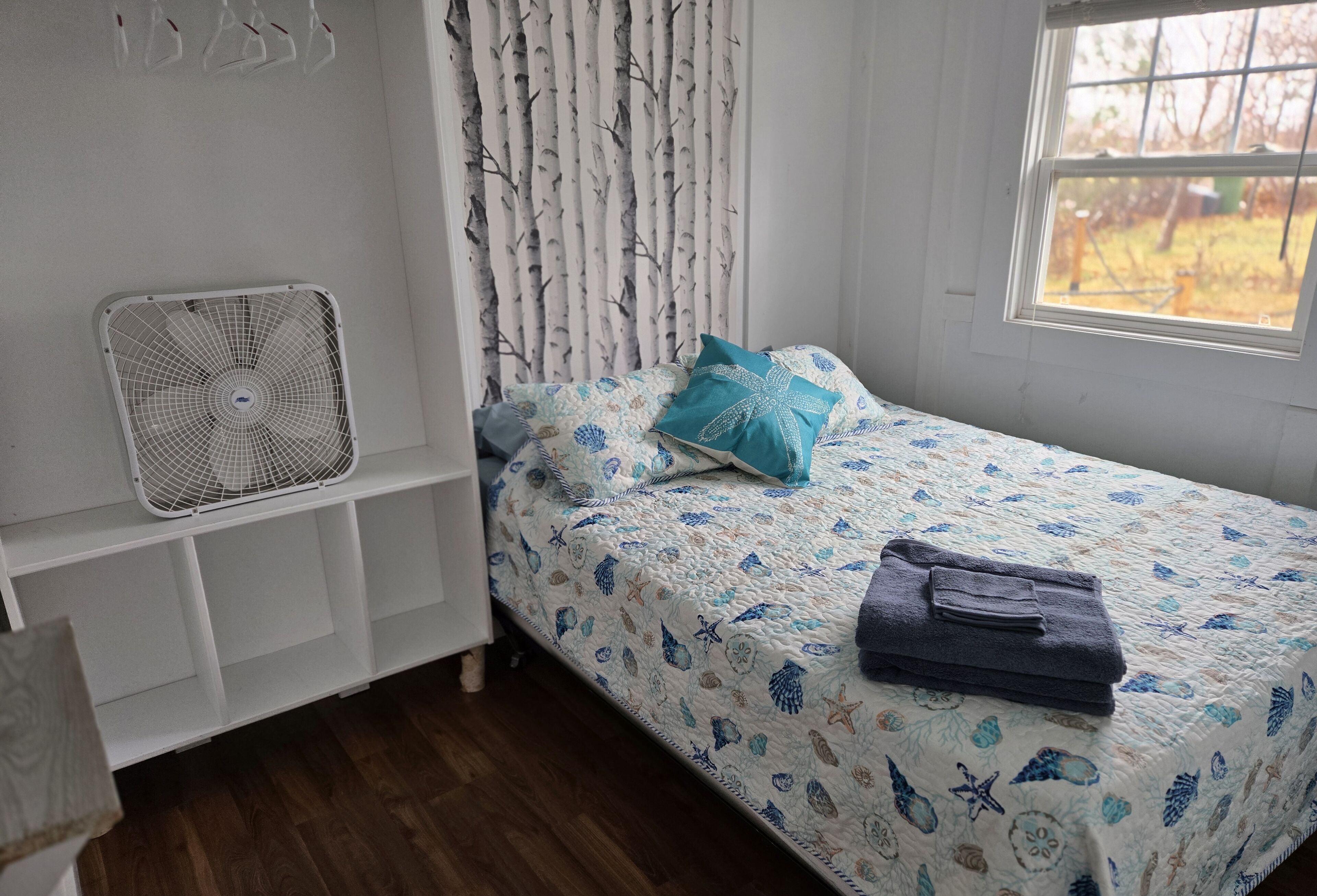 Un dormitorio con cama, ventilador, ventana y cortina.