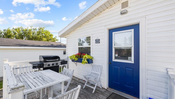 Een wit gebouw met een blauwe deur, een barbecue en buiten zitplaatsen.