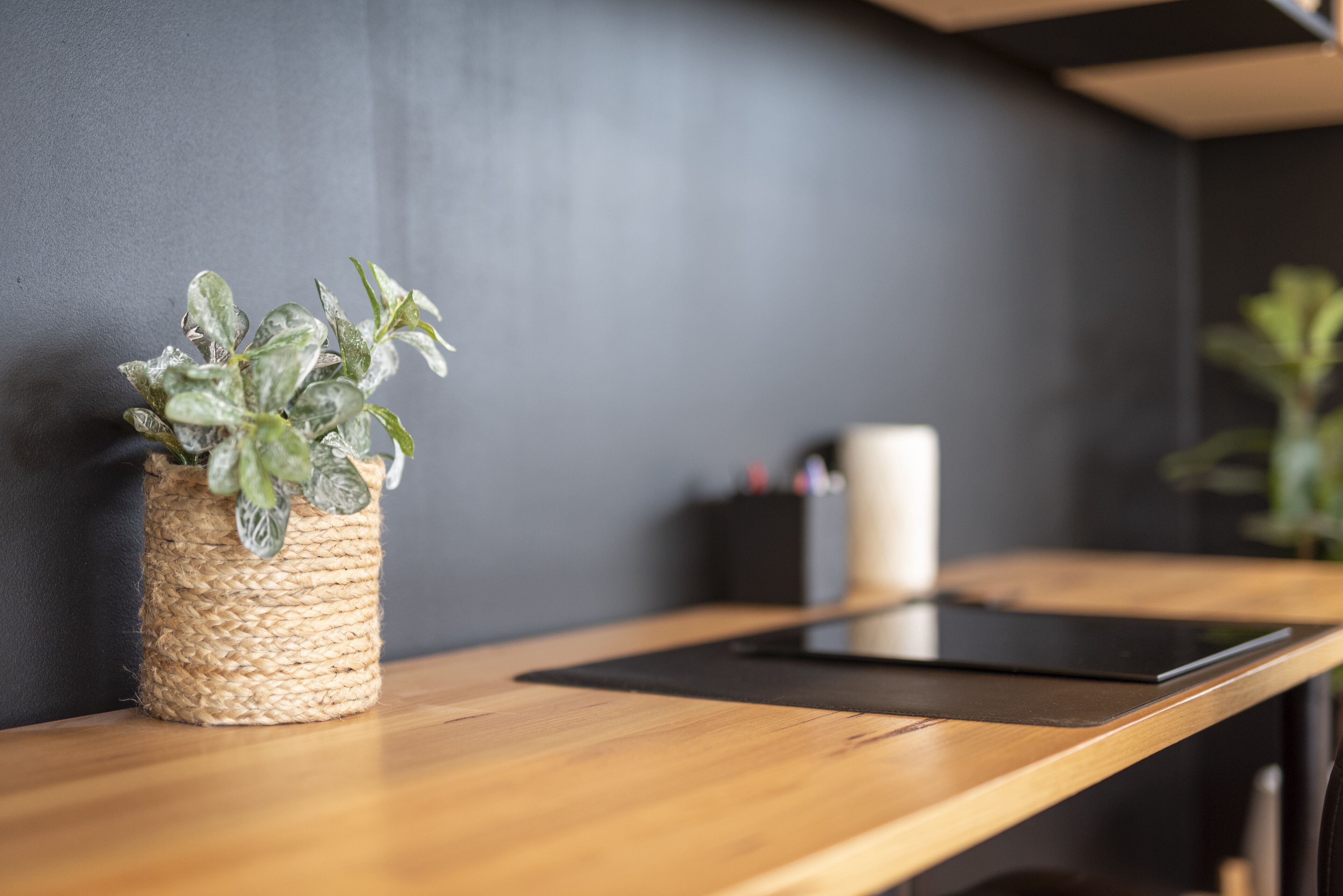 A wooden table with a woven basket containing a plant, a black tablet, and a black container with pens.
