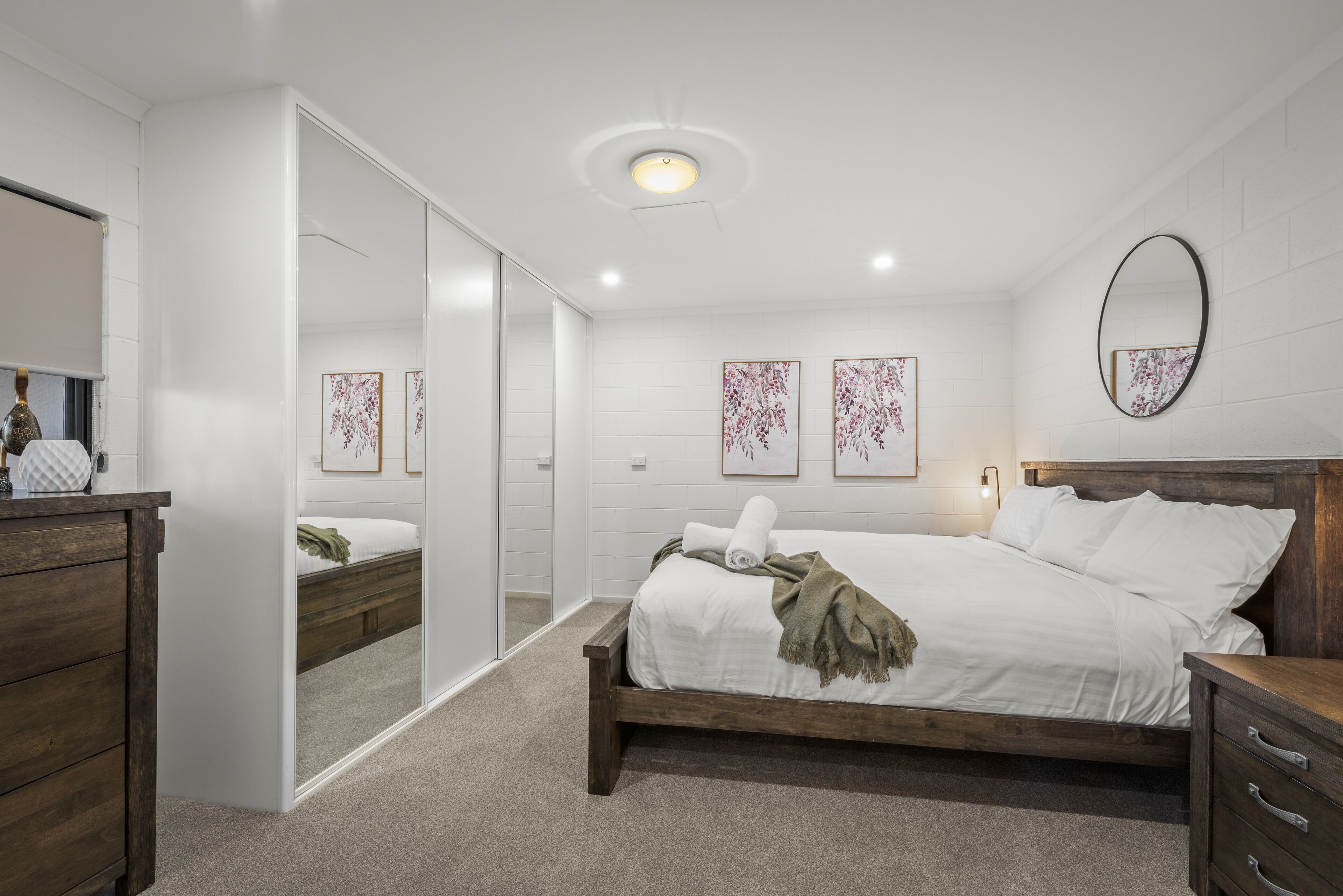 Ein Schlafzimmer mit einem hölzernen Bett, weißen Wänden, einem Spiegel und Kunstwerken.