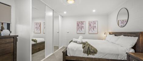 Ein Schlafzimmer mit einem hölzernen Bett, weißen Wänden, einem Spiegel und Kunstwerken.