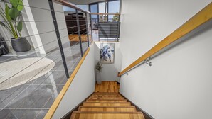 A modern staircase with wooden steps and a glass railing, leading to a balcony with a view of the outdoors. - Tree Top Views - 4 Bedroom House (Rosetta)