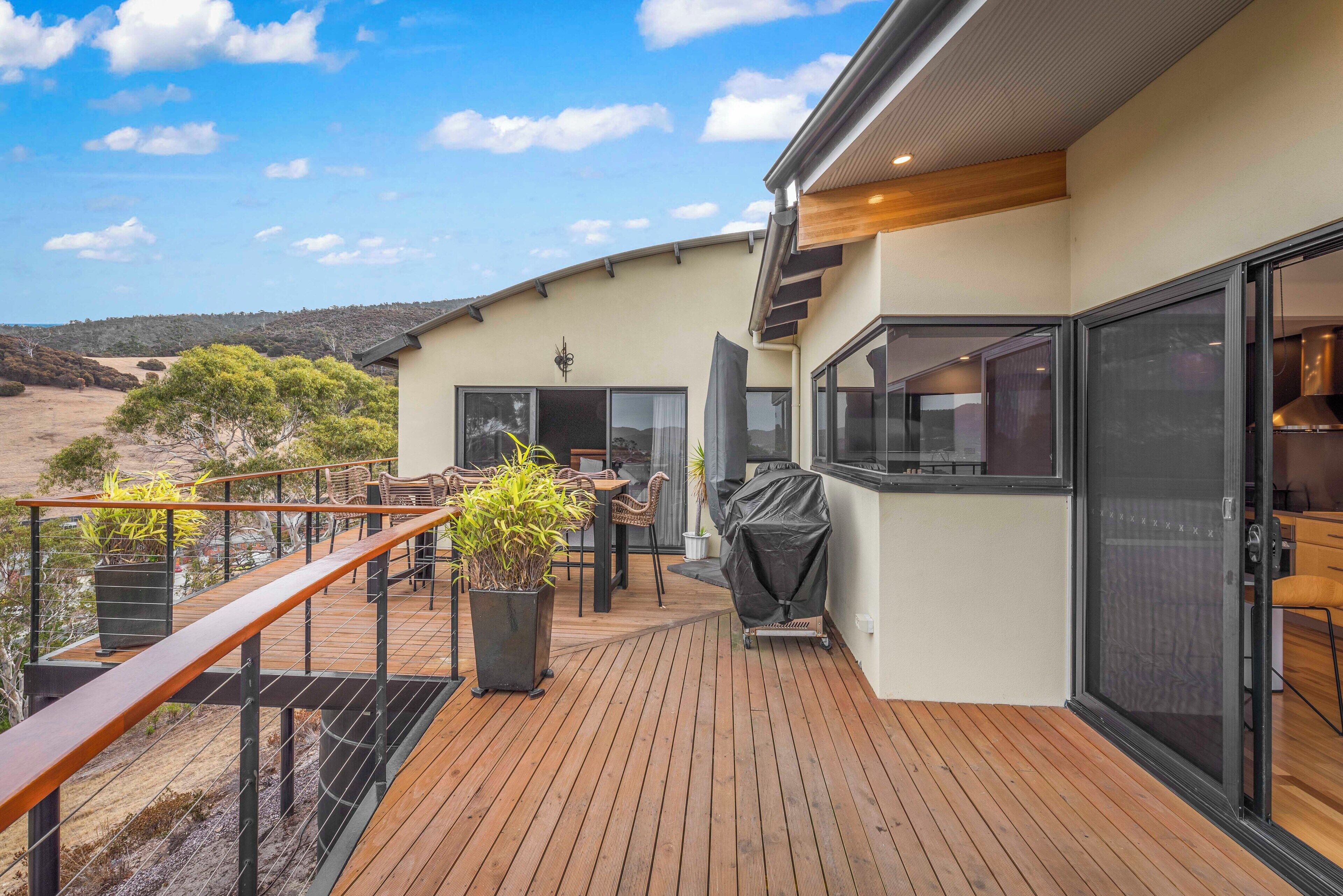 Une terrasse extérieure moderne avec un plancher en bois, un barbecue couvert et un espace détente comprenant des chaises et une table.