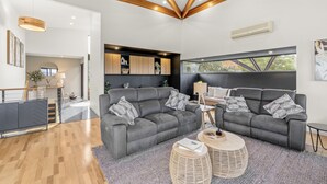 A modern living room with a grey sofa set, wooden ceiling beams, and a large window with a view. - Tree Top Views - 4 Bedroom House (Rosetta)