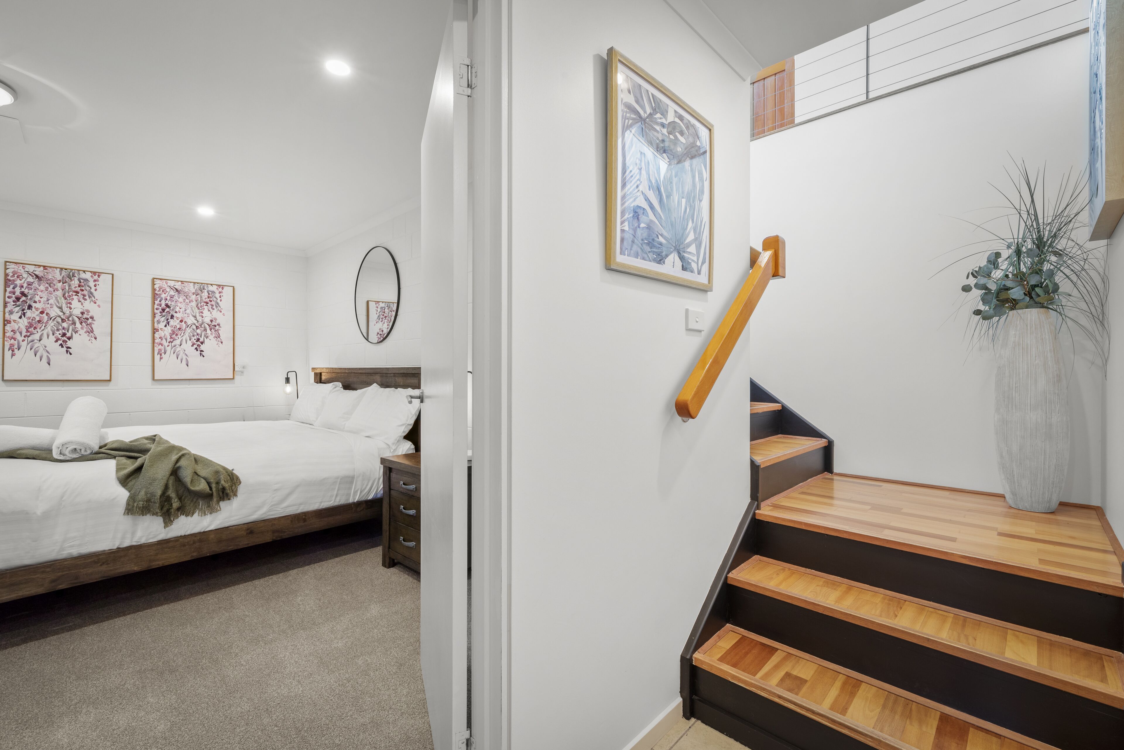 A bedroom with a bed, a nightstand, a dresser, and a staircase with wooden steps.