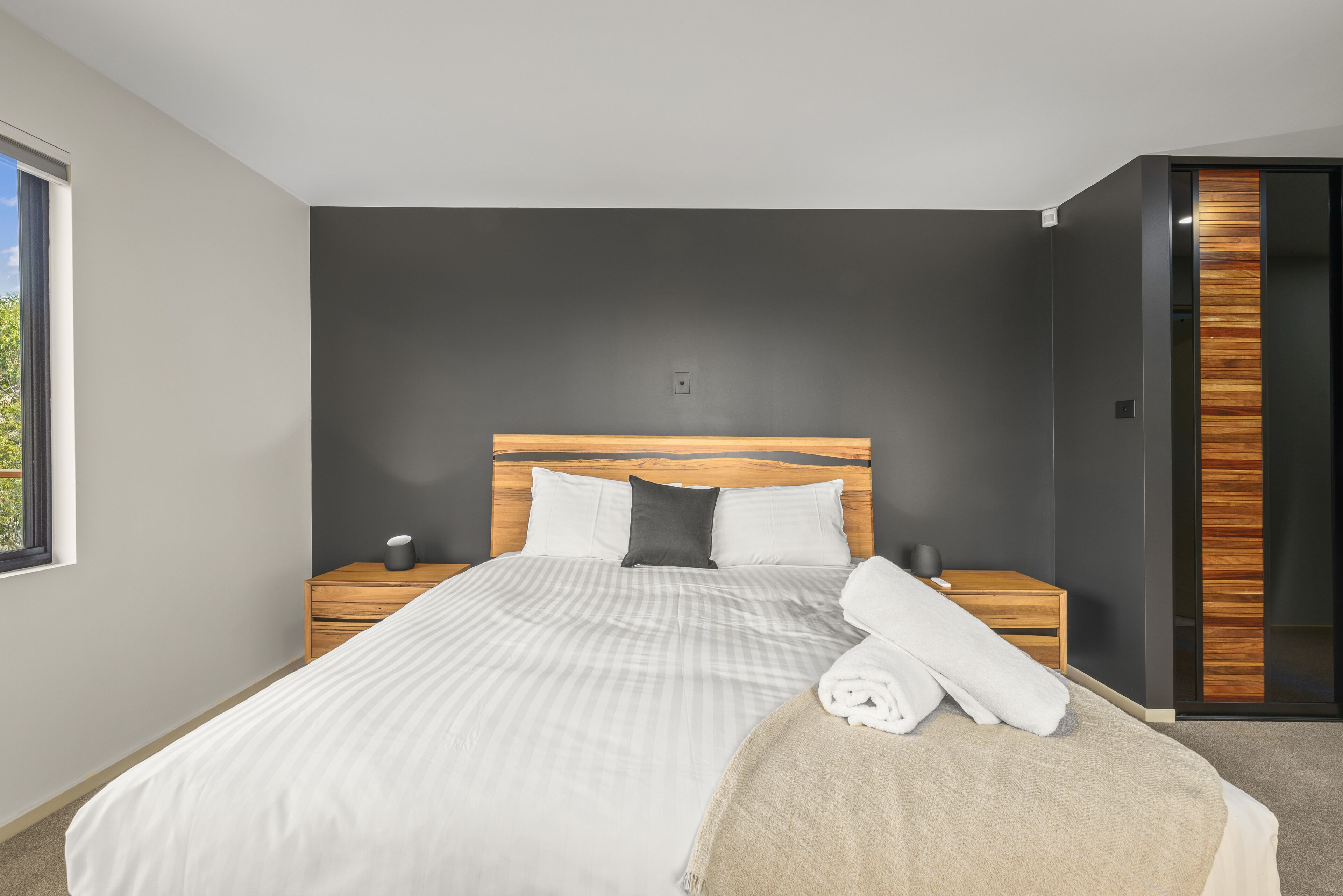 Un dormitorio moderno con una cama grande, cabecera de madera, dos mesitas de noche y una ventana.