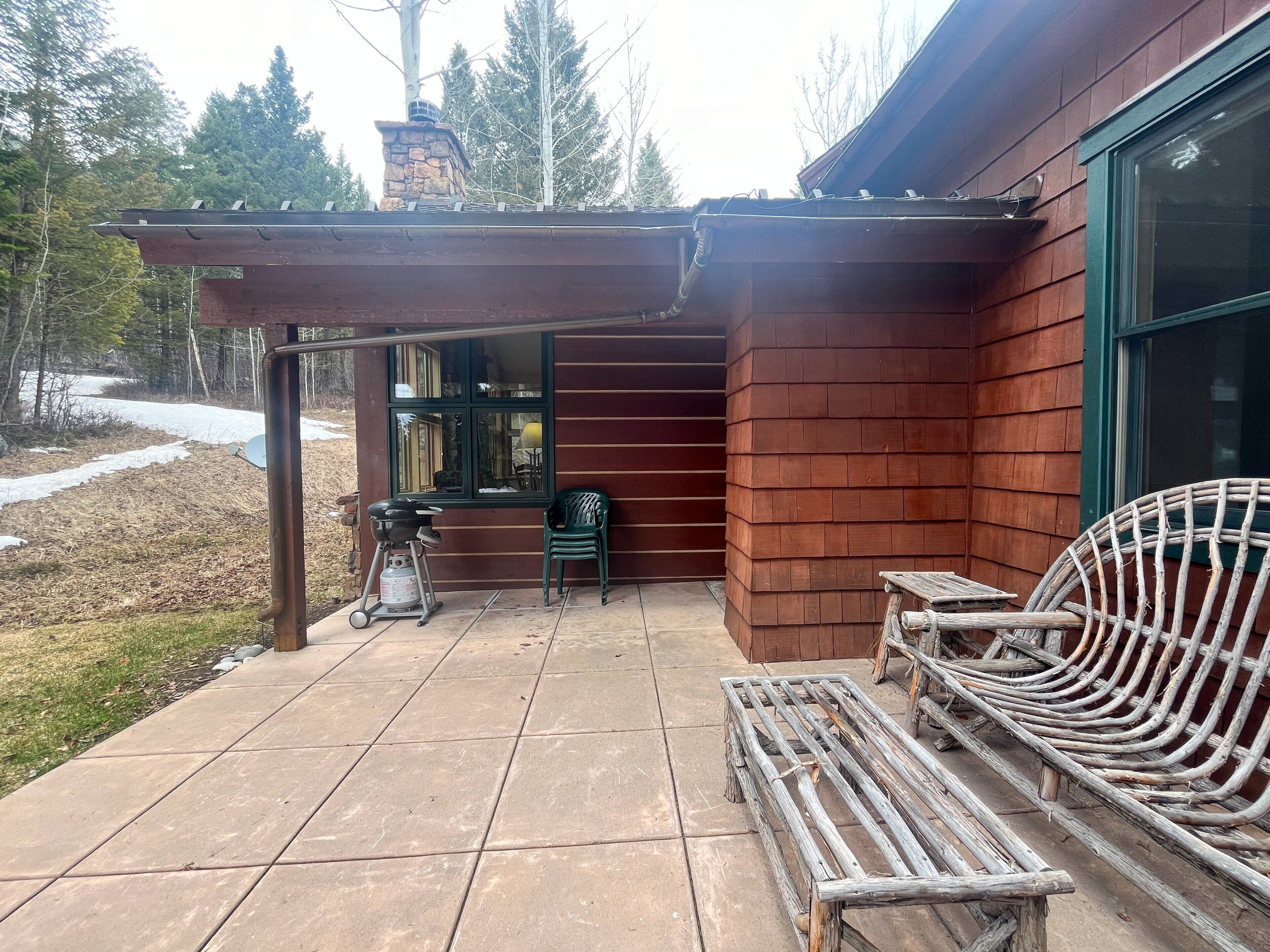 A patio with a grill, a chair, and a wooden bench.