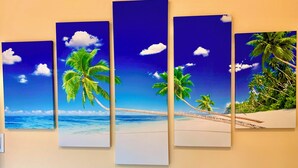 Un mur composé de quatre panneaux verticaux représentant une scène de plage avec des palmiers et l’océan.