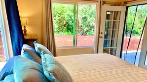 Une chambre à coucher avec un lit, des oreillers, une table de chevet, une lampe et une vue sur la verdure par la fenêtre.
