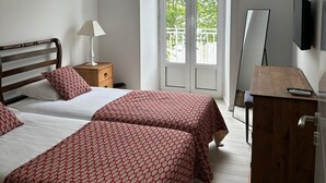 Una camera da letto con due letti, un comodino in legno, una scrivania, una TV e un balcone con vista sul verde.