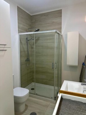 Ein modernes Badezimmer mit einer gläsernen Duschkabine, einer weißen Toilette und einem Holzwaschtisch.