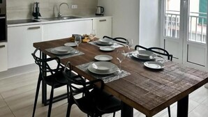 Una cucina moderna con mobili bianchi, un tavolo da pranzo in legno apparecchiato per quattro persone e un'ampia finestra che offre vista sull'esterno.