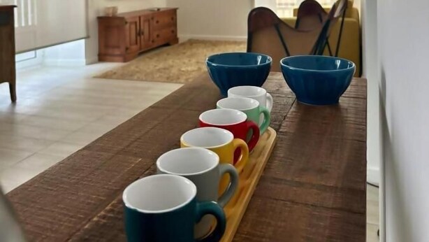 Un soggiorno moderno con un tavolino in legno che contiene tazze colorate, un televisore a parete e un'ampia finestra.