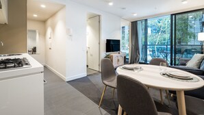 A modern kitchen with a gas stove, a dining area with a table and chairs, and a living area with a sofa and a TV. - StayCentral - Oasis on Mackenzie (Melbourne)