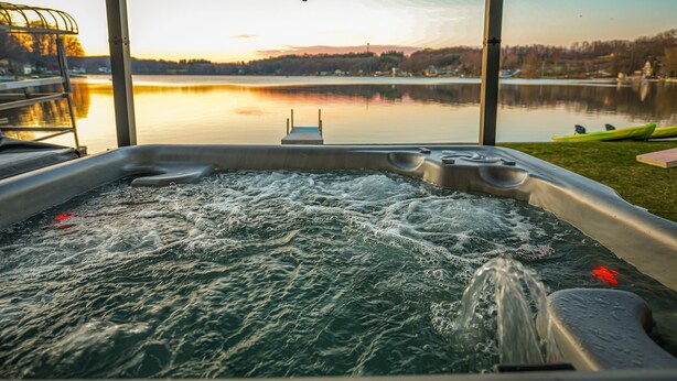 A hot tub with a view of a calm lake and distant hills during sunset.