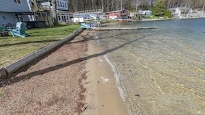 A lakeside property with a sandy beach, a dock, and houses in the background.