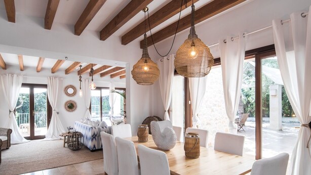 A spacious dining area with a wooden table and white chairs, surrounded by large windows and white curtains. - Pula Green- Villa with private pool and close to the beach (Son Servera)