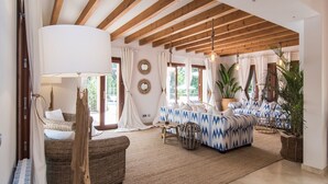 A spacious living room with a high ceiling, wooden beams, a large sofa, a wicker chair, and a dining area with a table and chairs. - Pula Green- Villa with private pool and close to the beach (Son Servera)