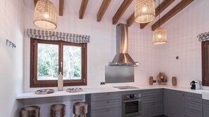 A modern kitchen with grey cabinets, a stainless steel range hood, and a large window with a view of greenery. - Pula Green- Villa with private pool and close to the beach (Son Servera)