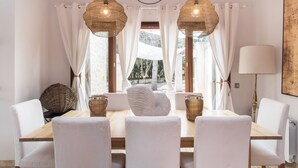 A dining area with a wooden table, white chairs, and two hanging wicker lamps. - Pula Green- Villa with private pool and close to the beach (Son Servera)