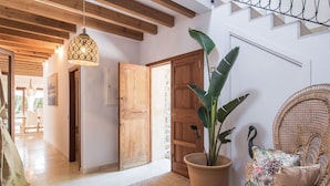 A spacious room with a wooden ceiling, a large potted plant, a wicker chair, and a hanging light fixture. - Pula Green- Villa with private pool and close to the beach (Son Servera)